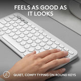 White keyboard with round keys on a desk, hand typing